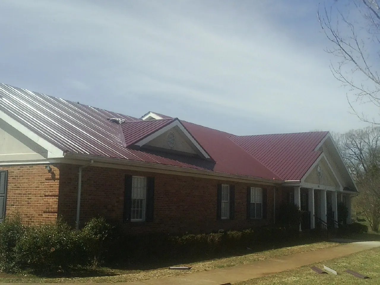 Red metal roof with gabled entries on a long brick building, from a Hail Damage Roof Repair job in Nokomis