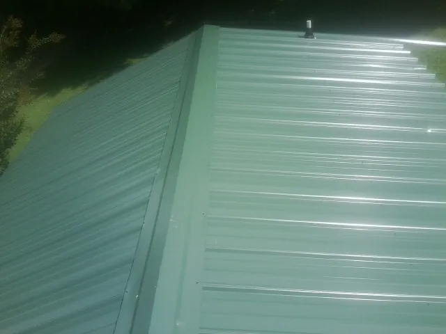 New green metal panels meeting at the ridge of a roof — Flat Roof Repair work by our crew in Nokomis