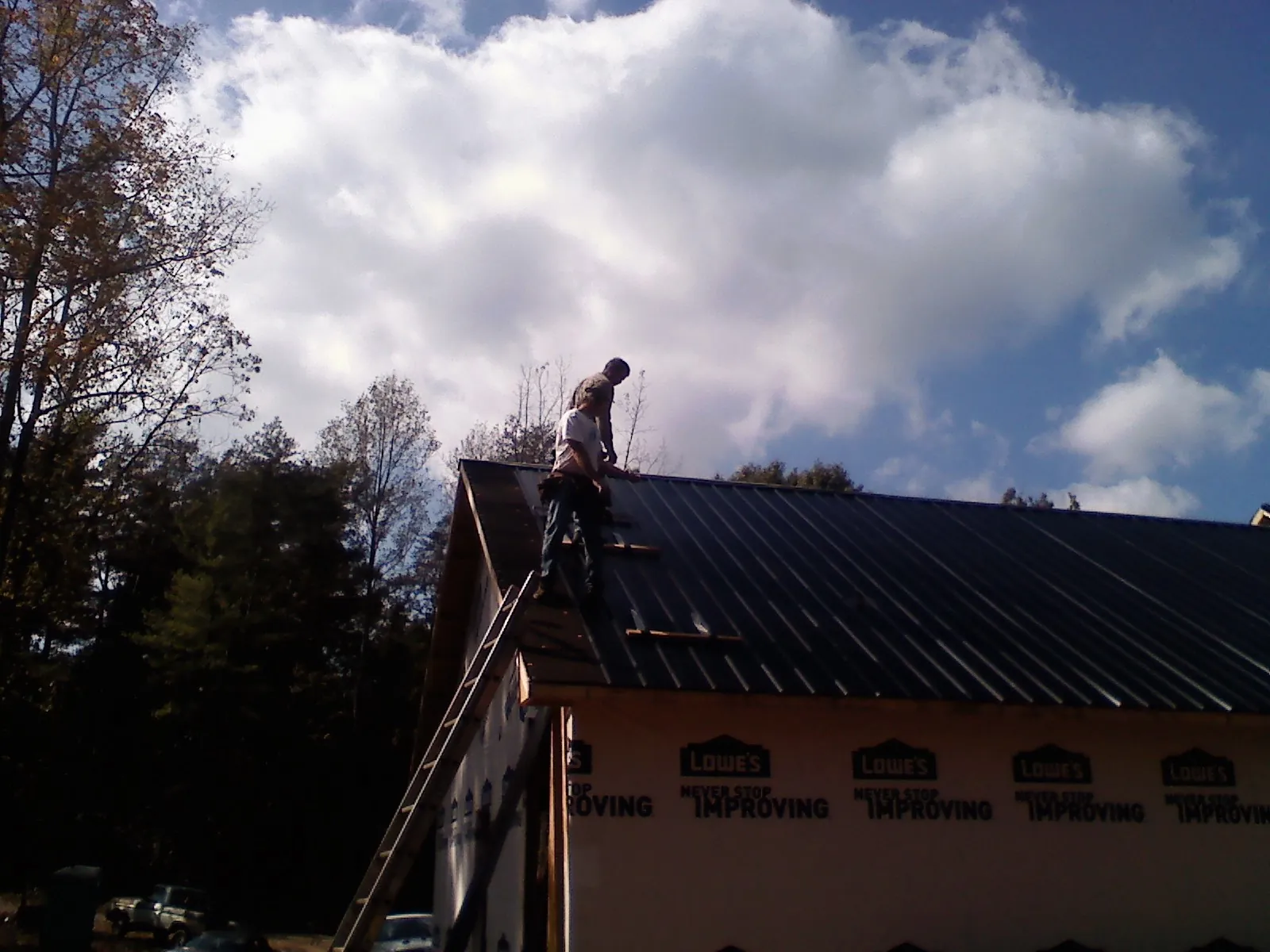 Roofer fastening dark metal panels high against a cloudy sky, from a Roof Inspection job in Nokomis