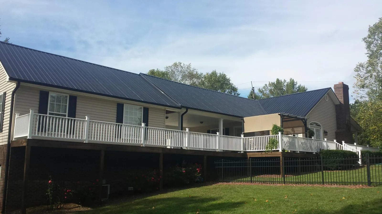 Black metal roof above a long white railed deck on a hillside home in Nokomis