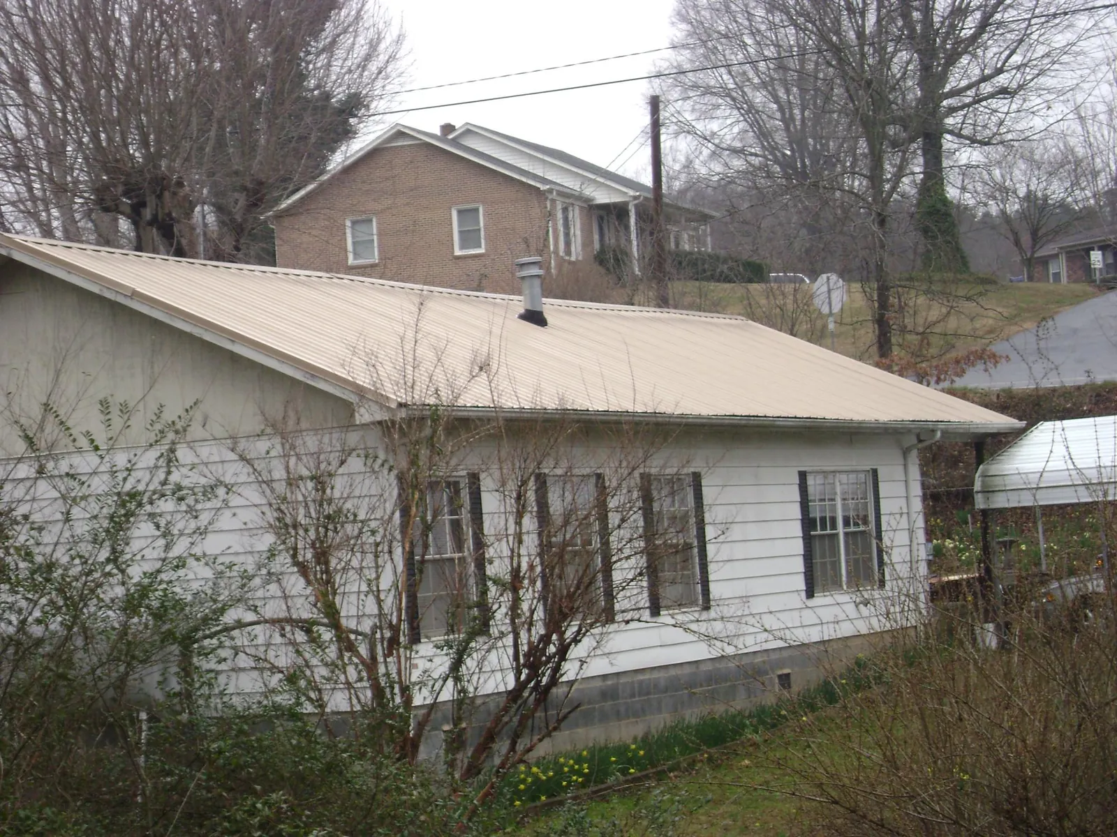 Tan metal roof on a white sided house set into a hillside — Commercial Roofing by Roofing Brothers in Nokomis